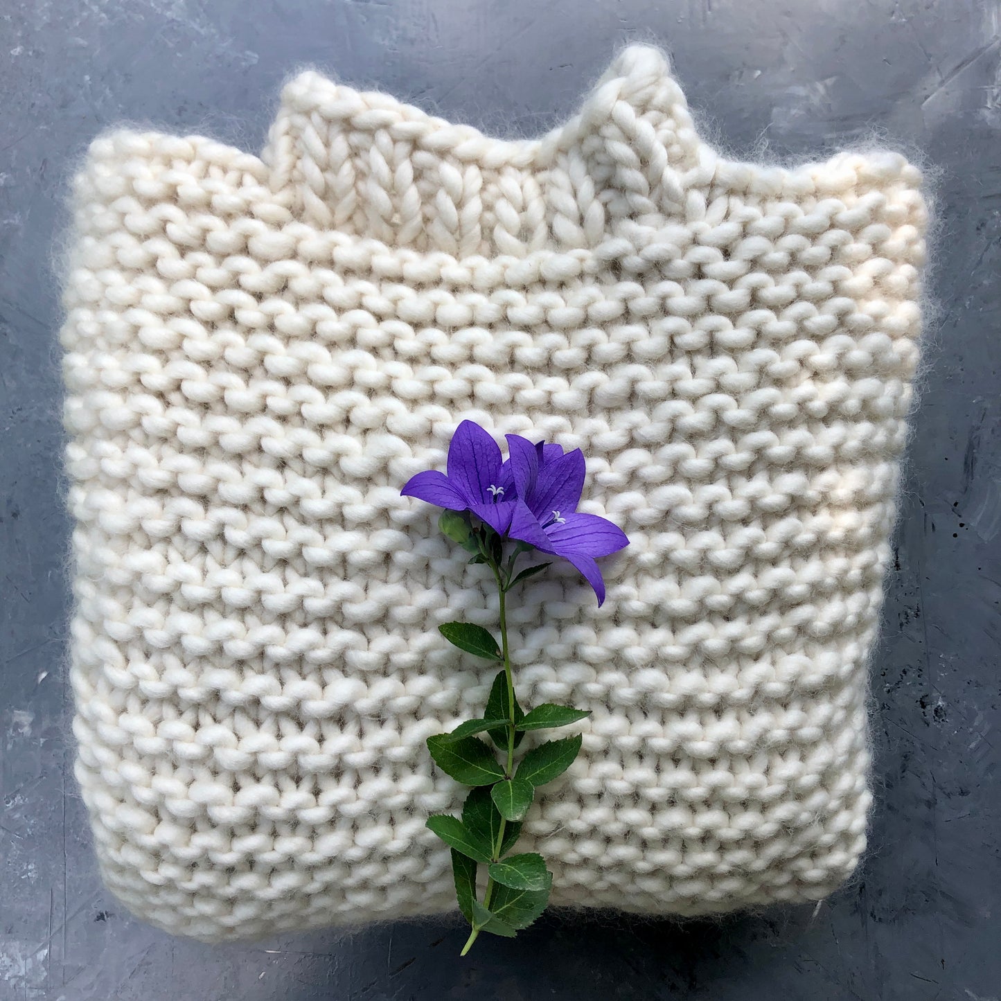 Folded Alaska Dream Sweater in creamy white chunky garter stitch, displayed on a dark surface.