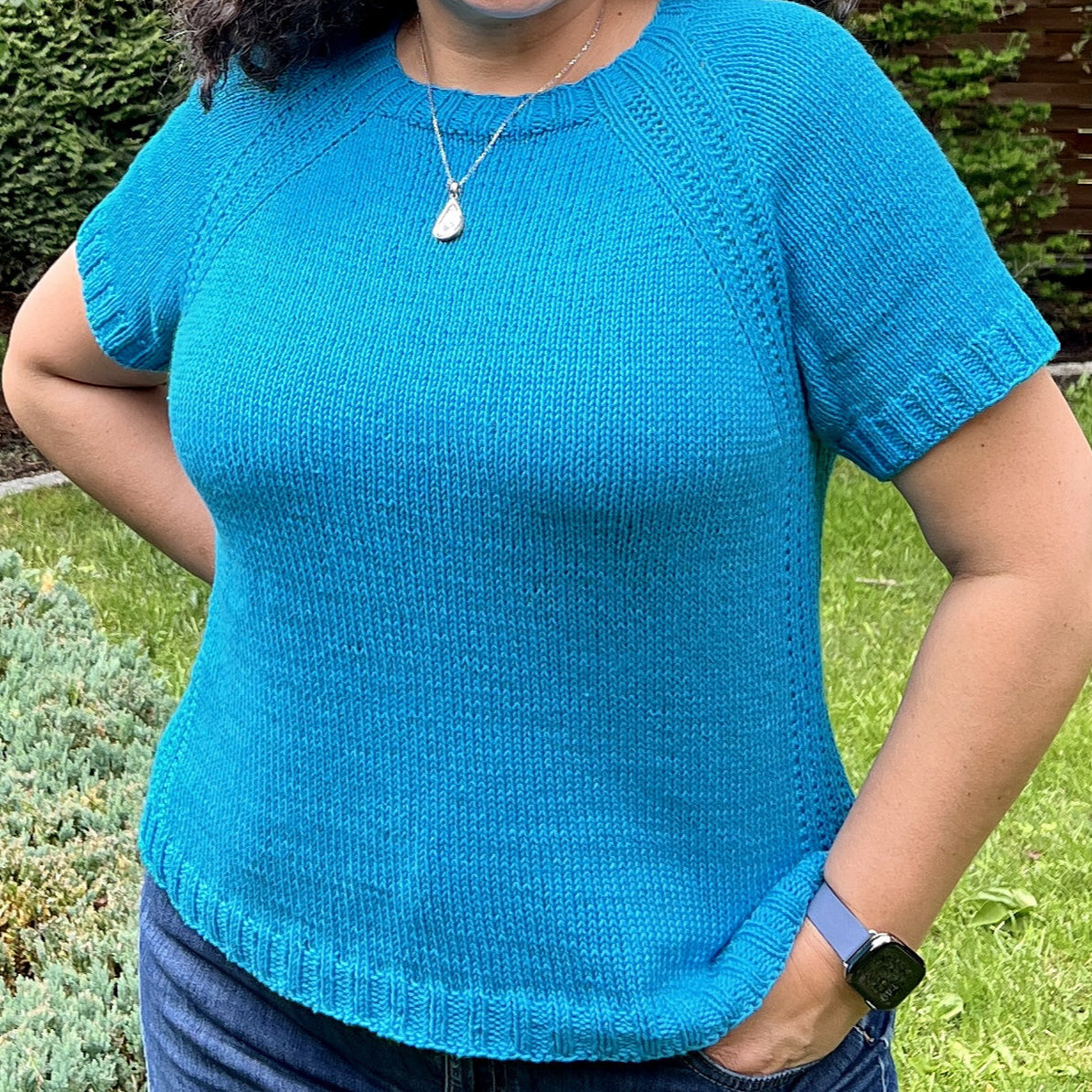 Person wearing a bright blue short-sleeved knit sweater with ribbed edges standing on green grass.