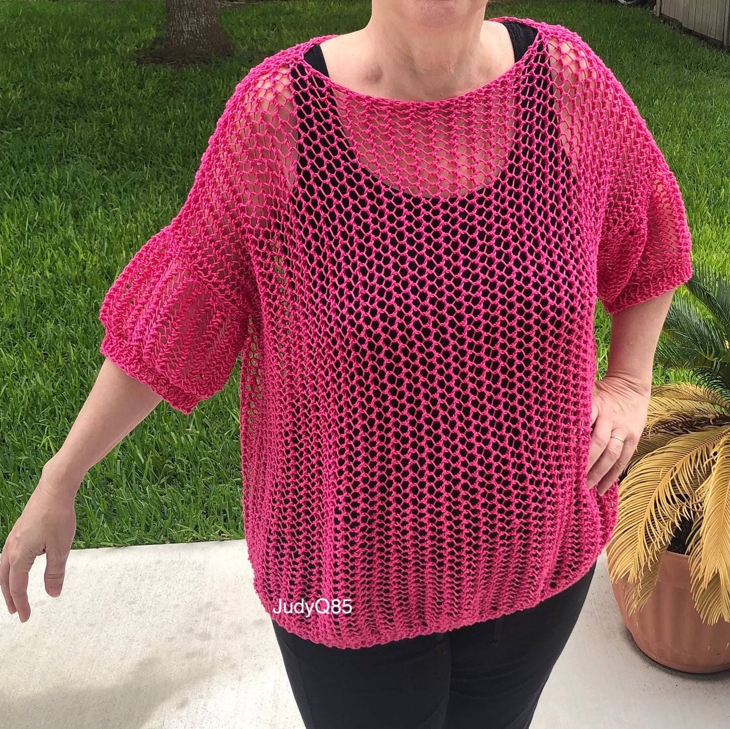 Person wearing a bright pink Halcyon Lace Sweater over a black tank top.