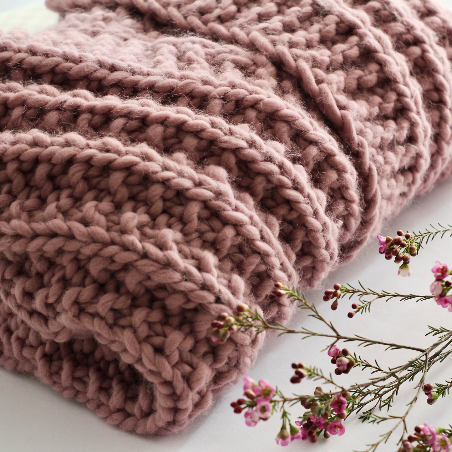 A folded chunky knit sweater in dusty rose, showcasing its thick textured stitches.