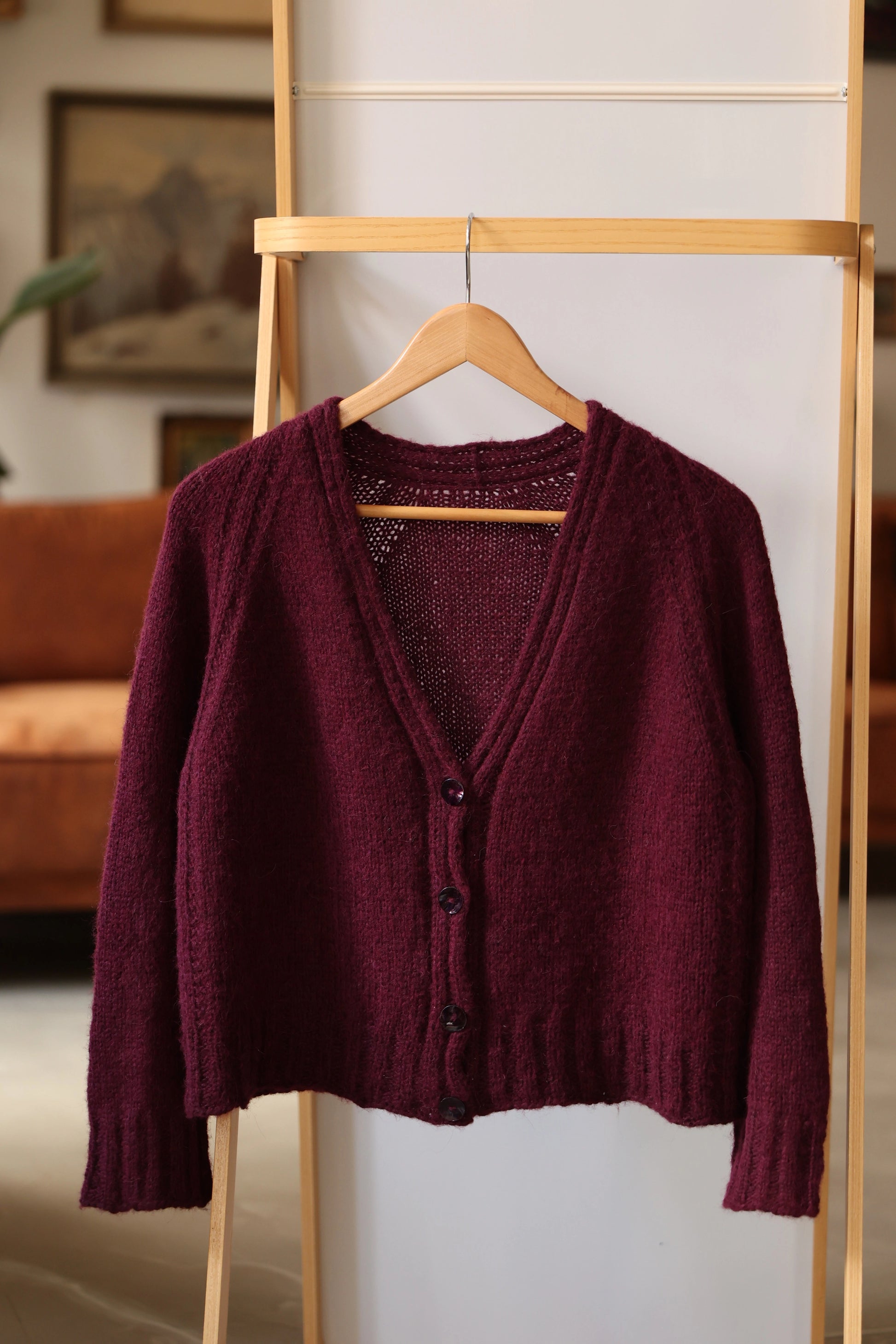 The Mellow Mood Cardigan in deep wine color hanging on a wooden rack