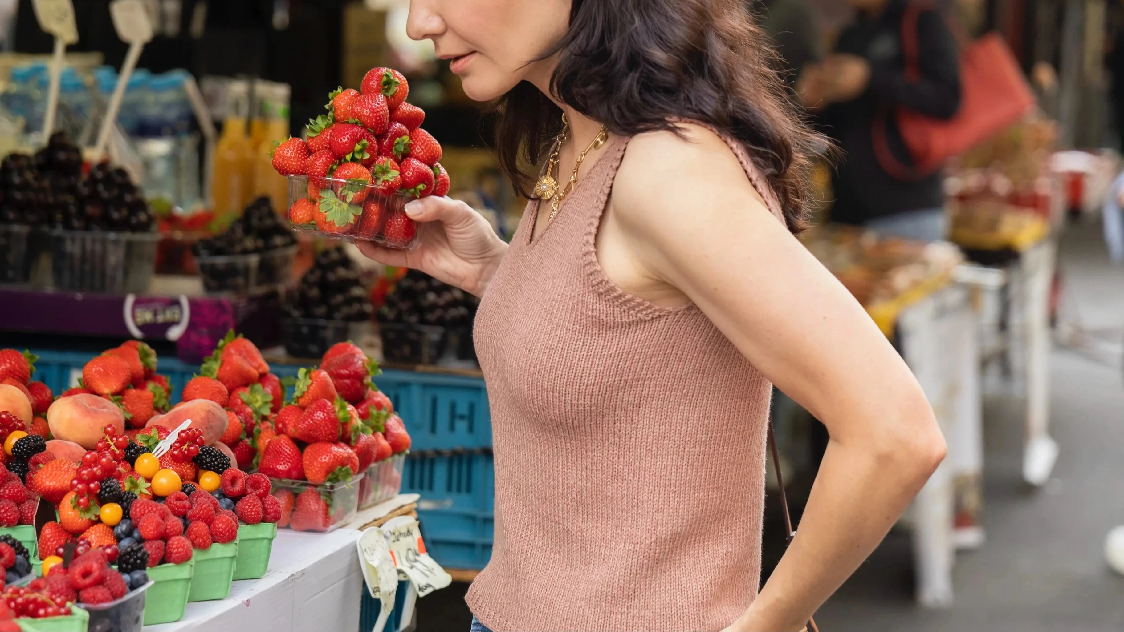 Woman in v-neck top holding a bowl of strawberries at an outdoor market.