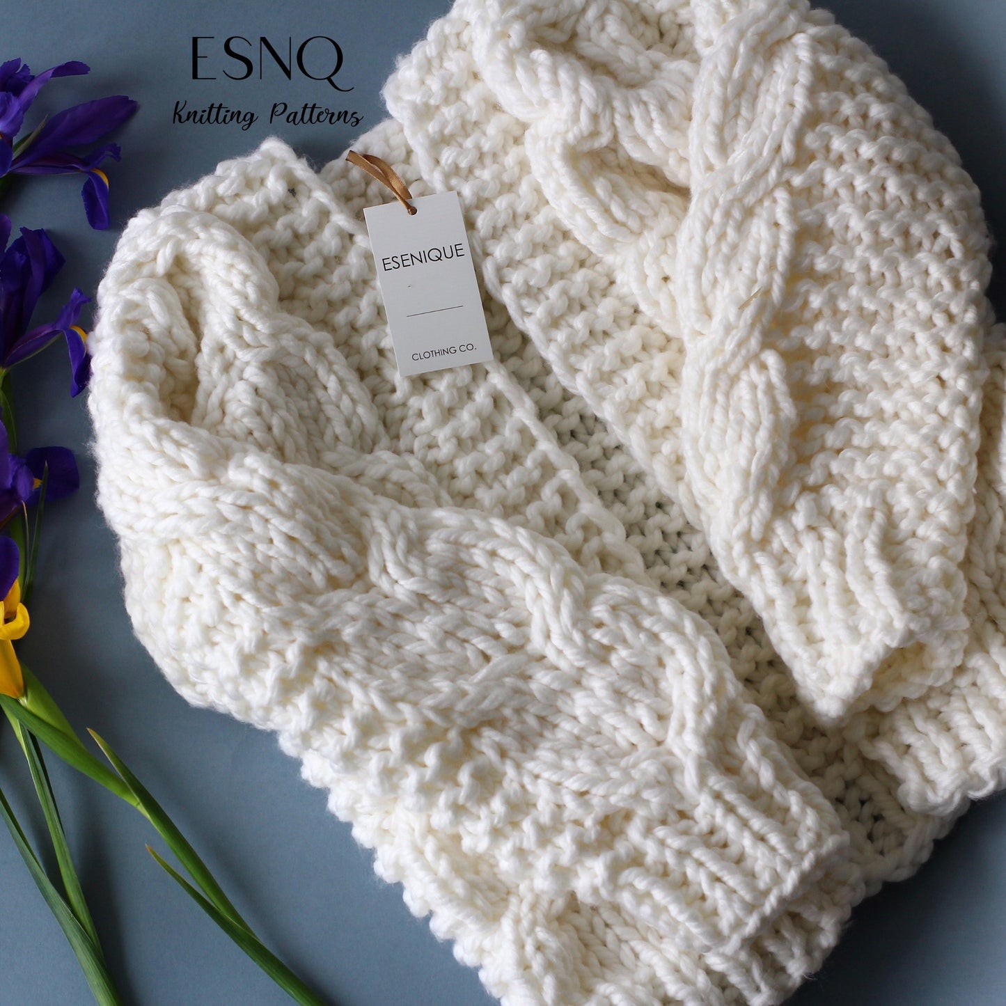 Folded Sequoia Cardigan in ivory with chunky cable knit detail, styled with fresh flowers and an ESENIQUE tag.