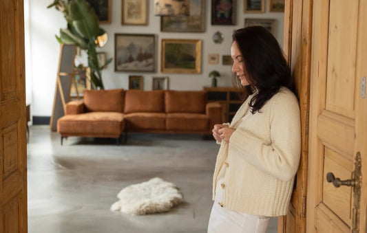 A woman leaning against a wooden wall, wearing the Mellow Mood Cardigan in cream with matching white pants