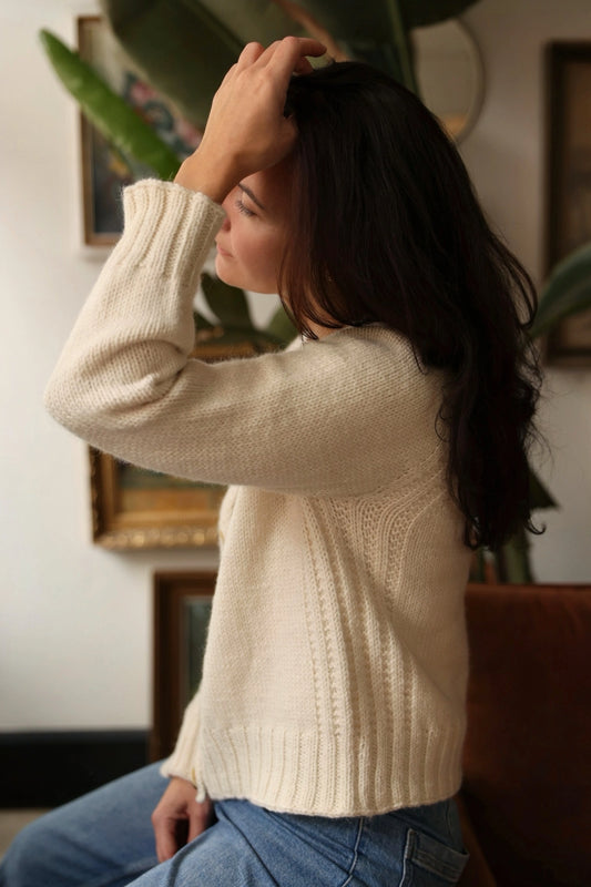 A woman wearing the Mellow Mood Cardigan in cream sits thoughtfully