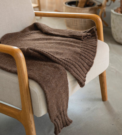 Brown knitted blanket draped over a beige chair in a cozy room.