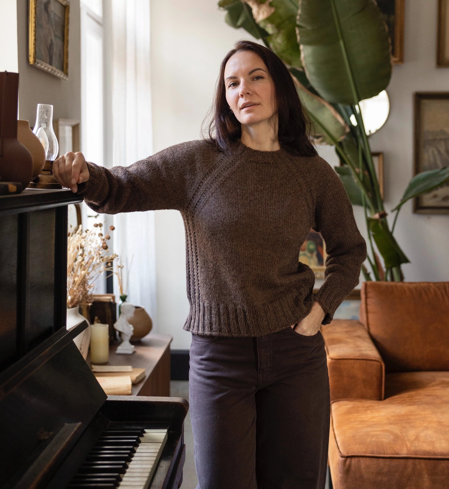 Woman in a brown sweater standing in a living room with a piano and sofa.