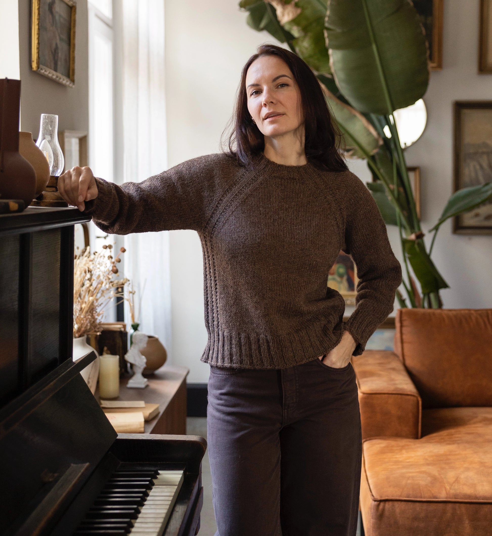 Woman in a brown sweater standing in a living room with a piano and sofa.