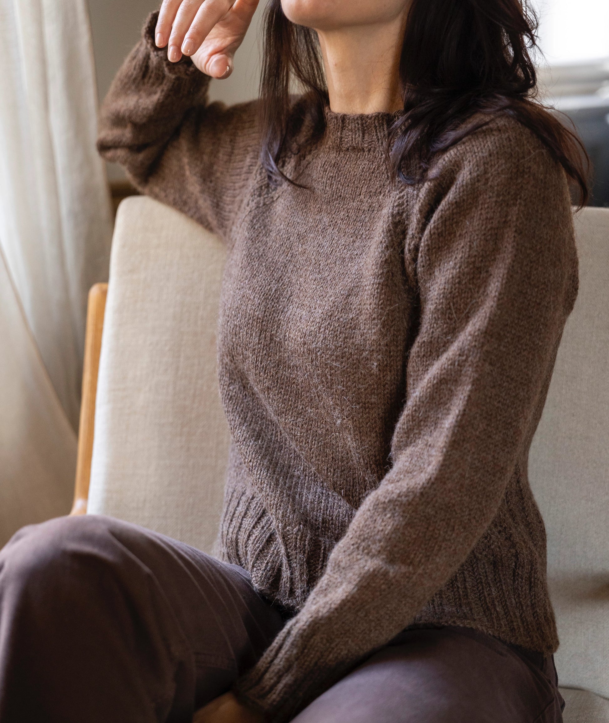 Person wearing a brown knitted sweater sitting on a couch.