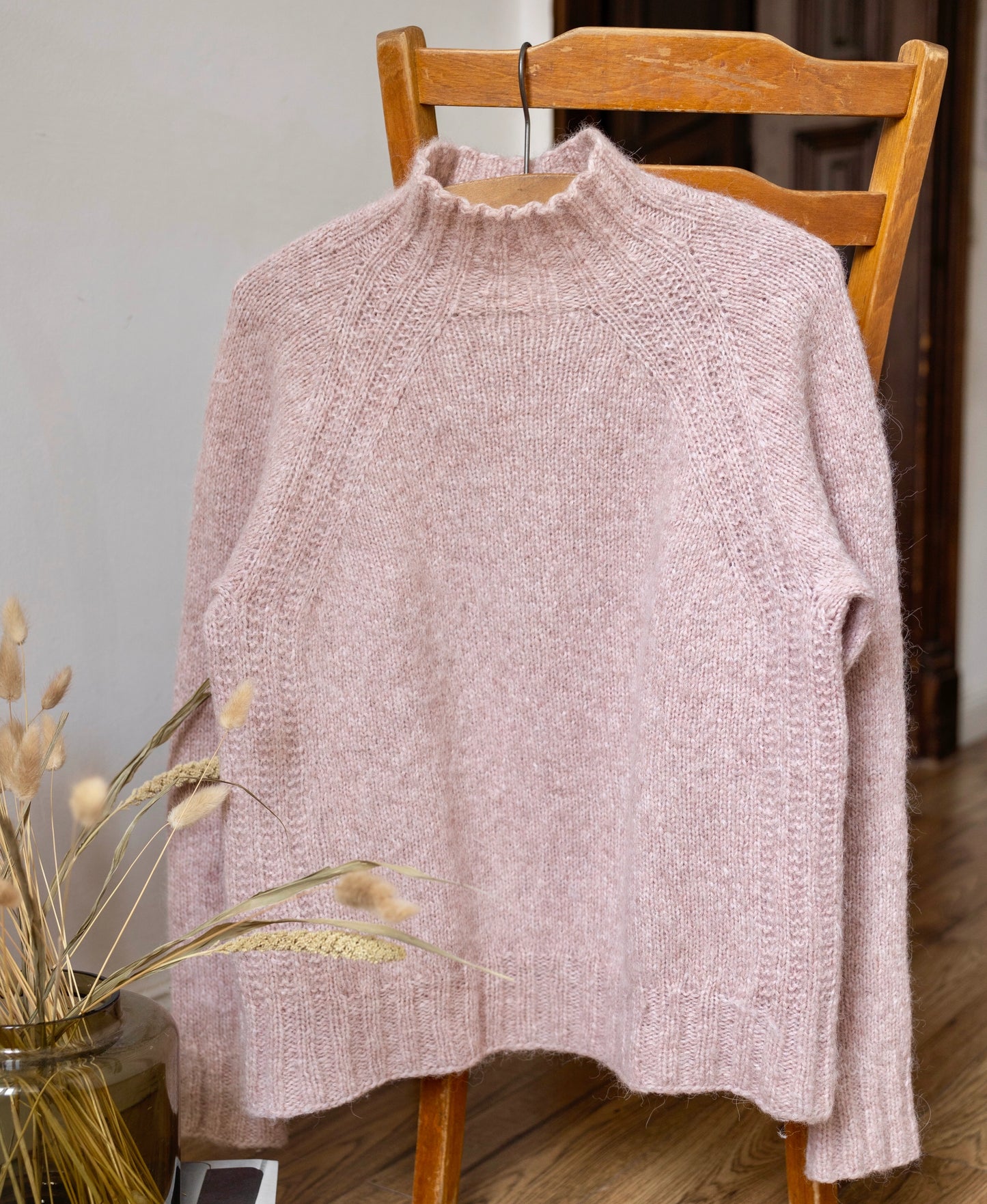 Pink sweater draped over a wooden chair with a neutral background
