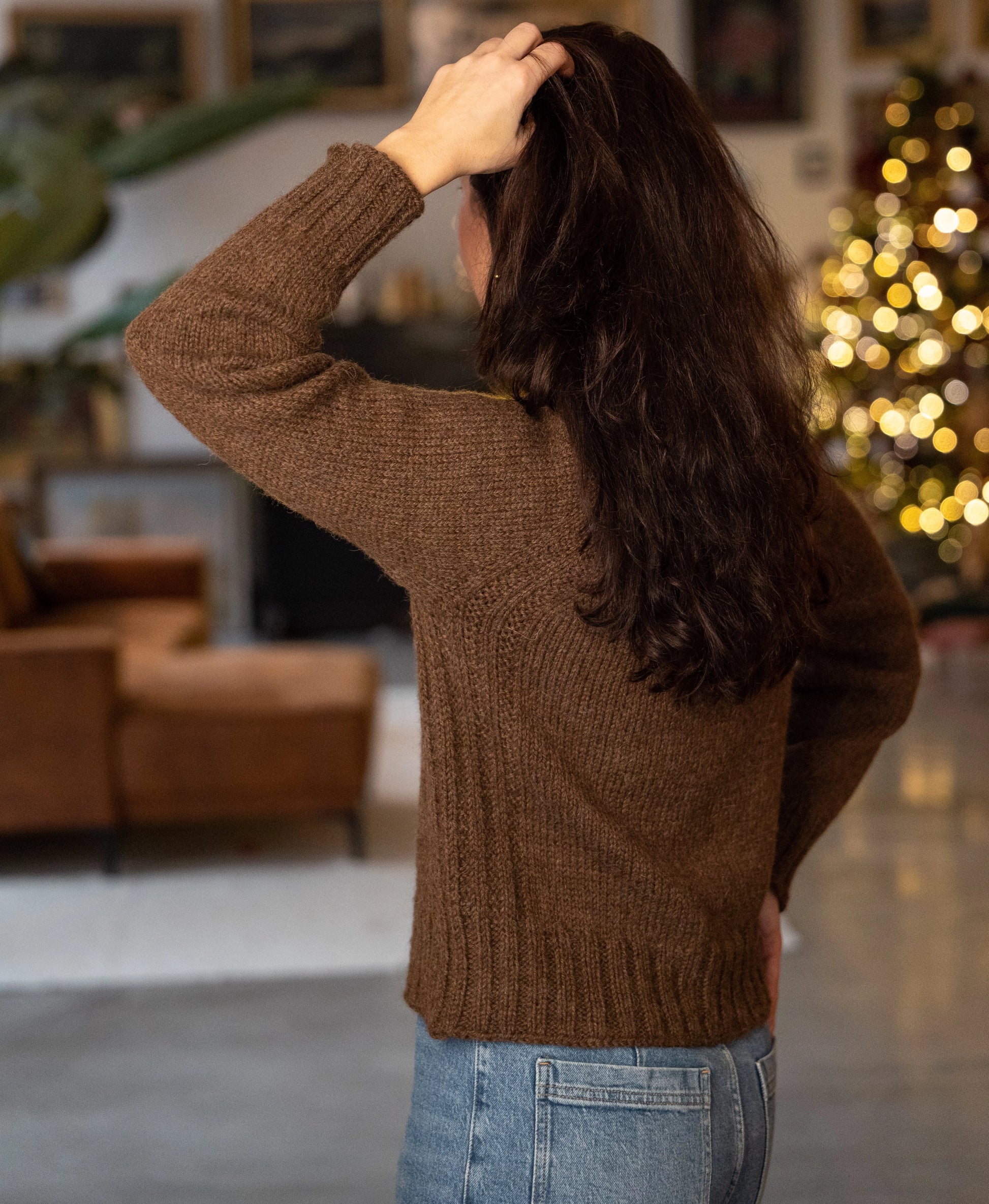 Person wearing a brown sweater in a room with a Christmas tree