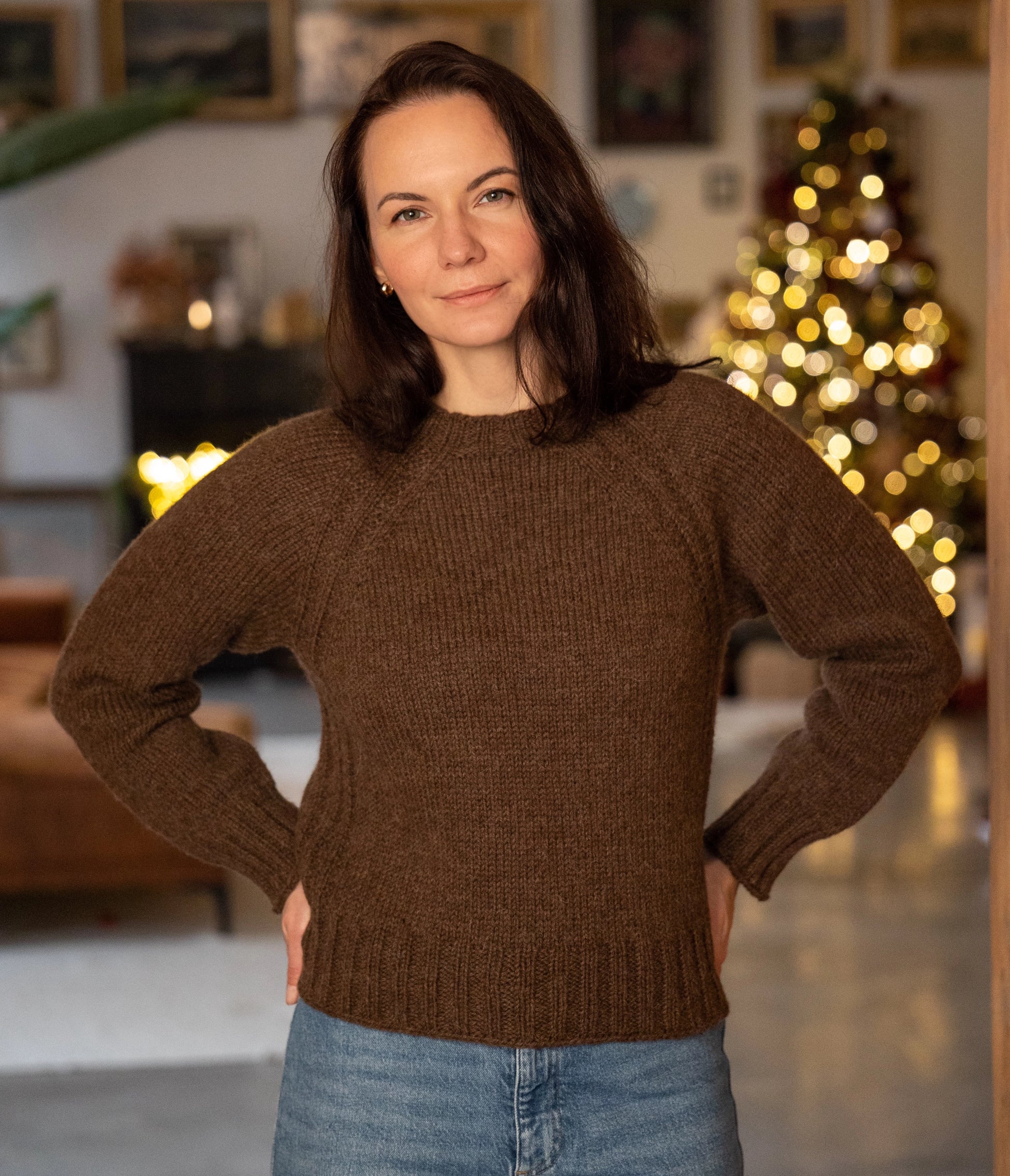 Woman wearing a brown sweater in a cozy living room with a Christmas tree.