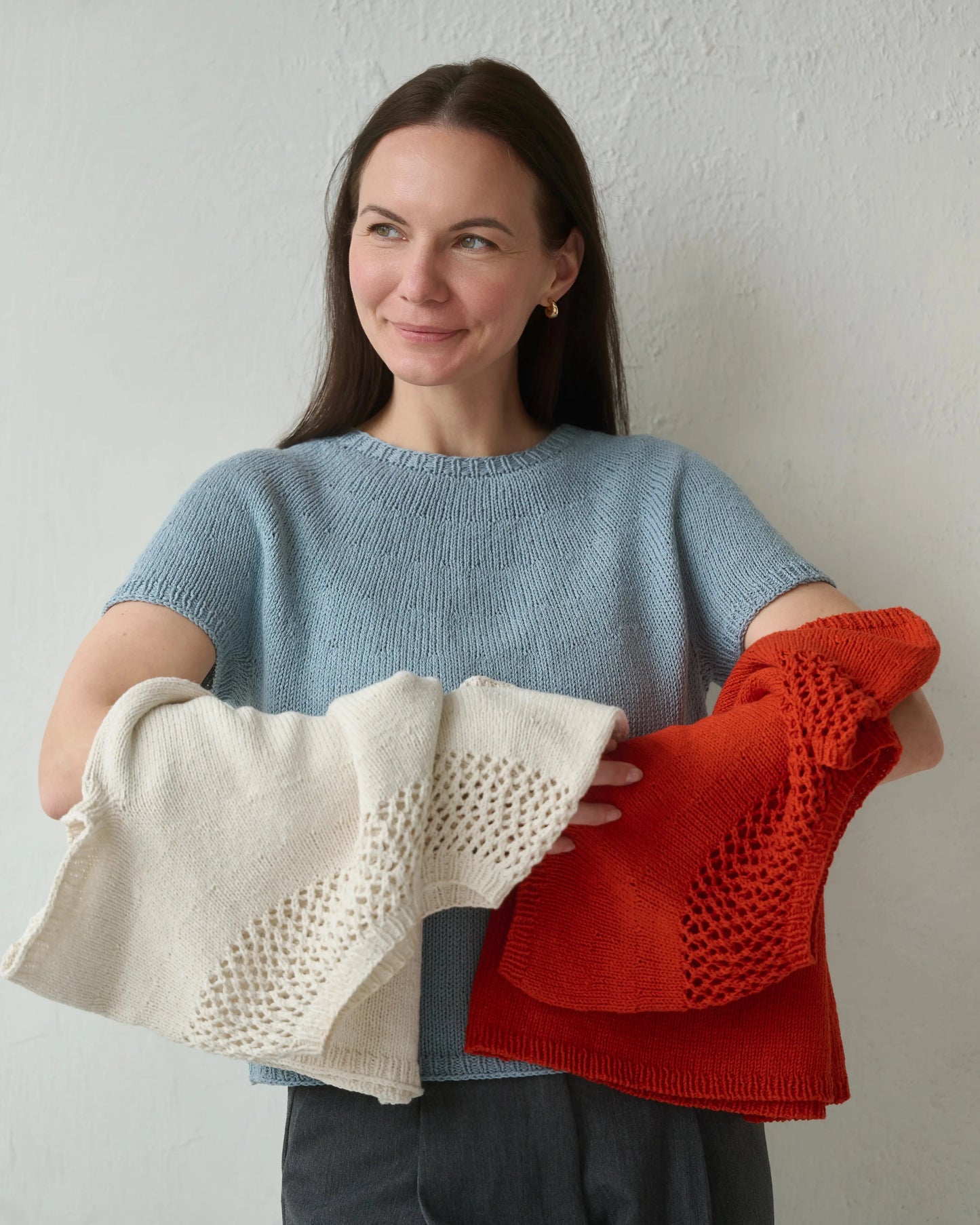Woman holding three knitted items in front of a plain background