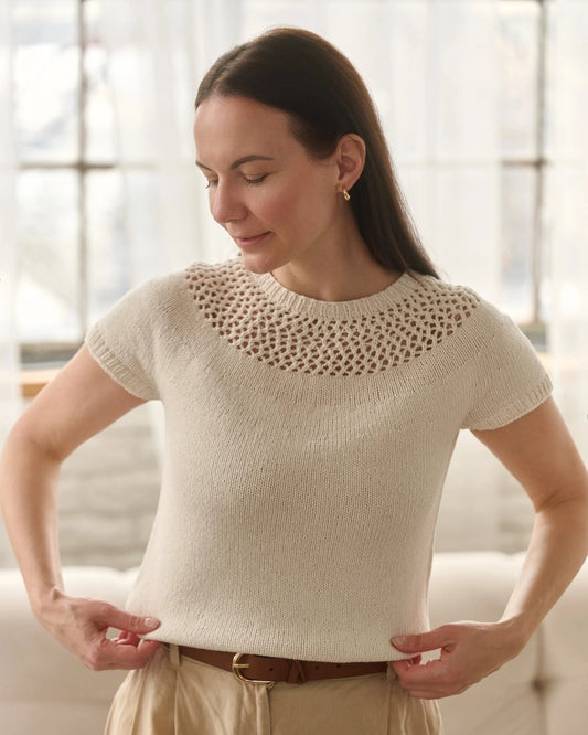 Woman wearing a beige knit top with a textured neckline in a bright room.