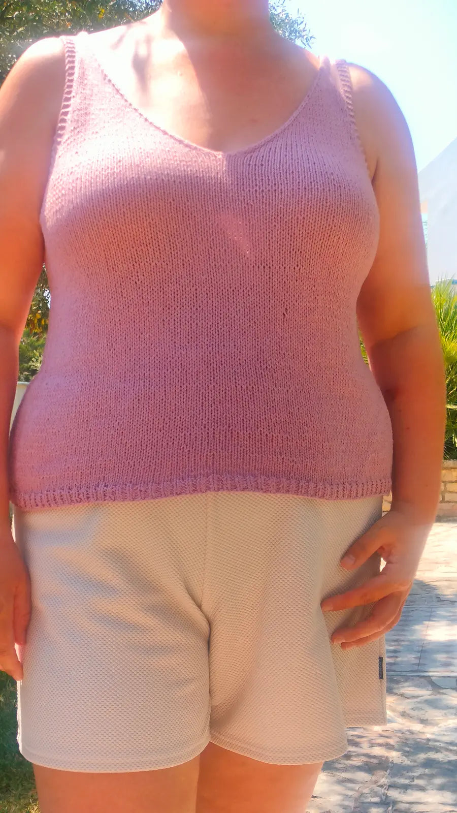 Person wearing a pink knitted tank top and beige shorts outdoors.