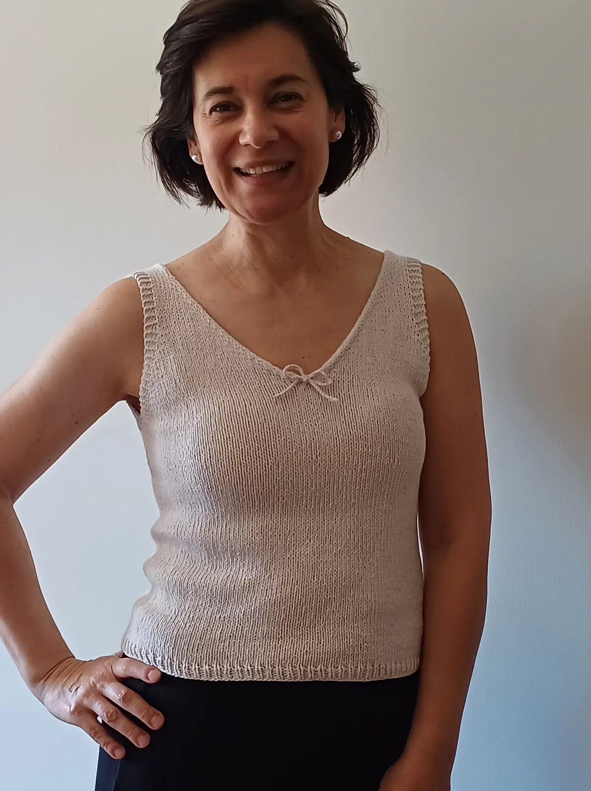Woman wearing a beige knitted tank top against a plain background