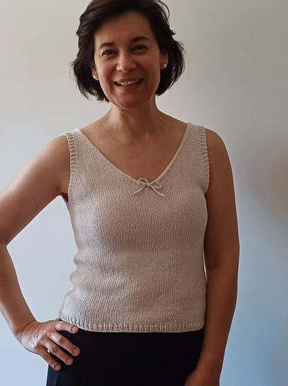 Woman wearing a beige knitted tank top against a plain background