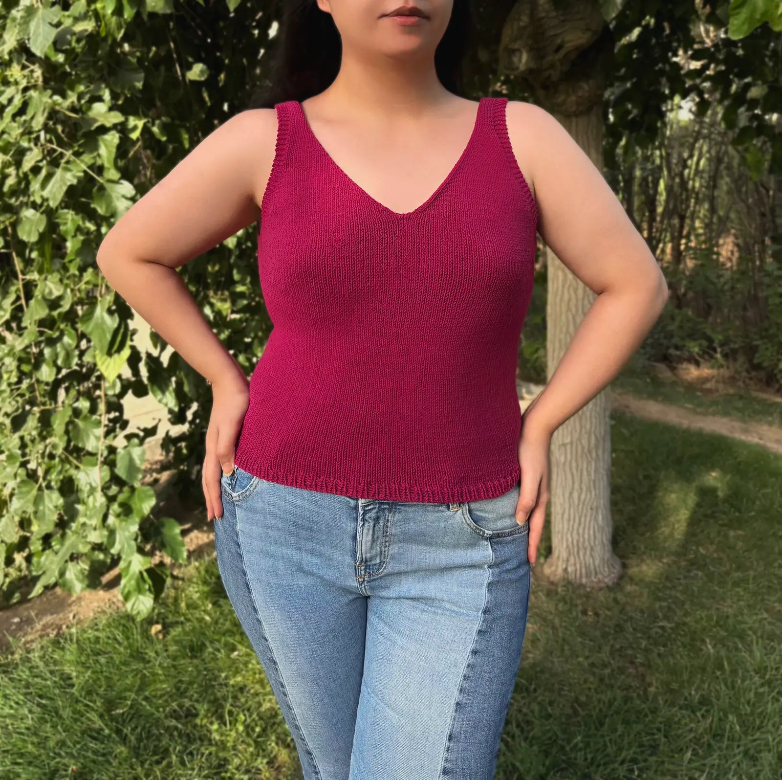 Person wearing a pink knitted tank top and blue jeans standing outdoors.
