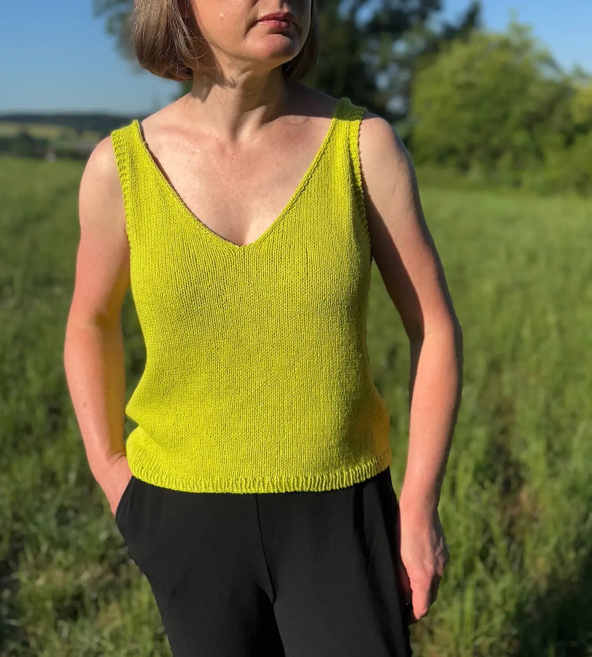 Person wearing a bright yellow sleeveless top standing in a grassy field.