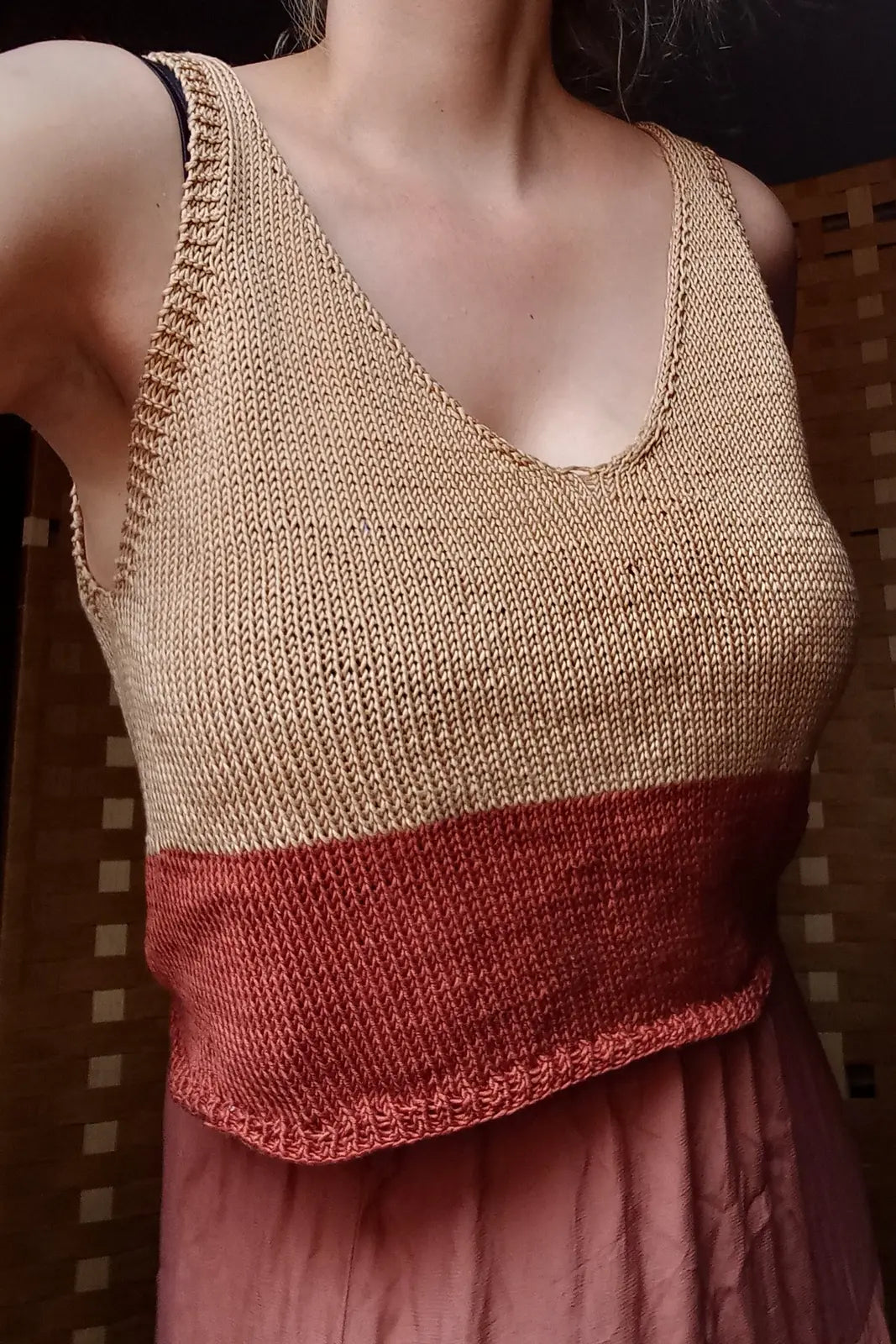 Person wearing a two-tone knitted tank top with beige and red colors.