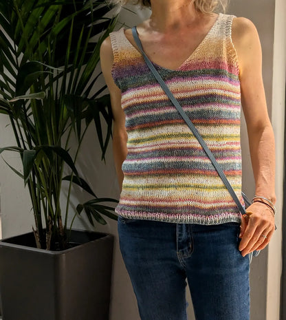 Person wearing a colorful striped sleeveless top standing next to a plant indoors.