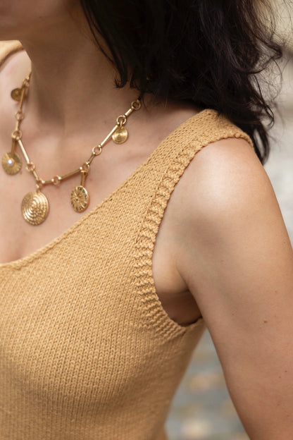 Woman wearing a beige sleeveless top and gold necklace with circular pendants.