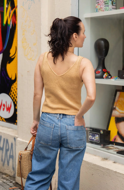 Woman in a yellow sleeveless top and blue jeans walking past a store window with colorful artwork.