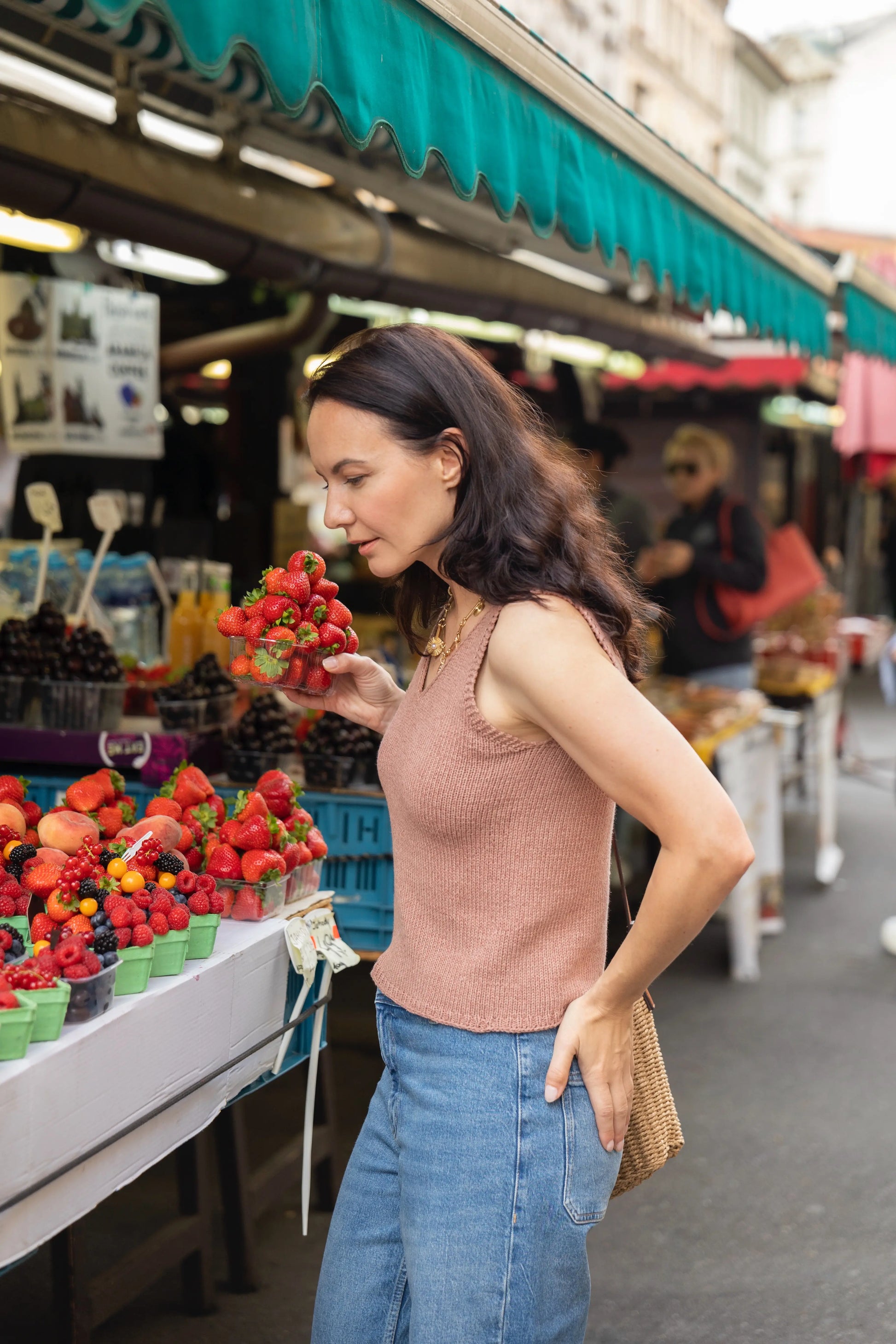 Woman shopping at an outdoor market with fruits and vegetables.
