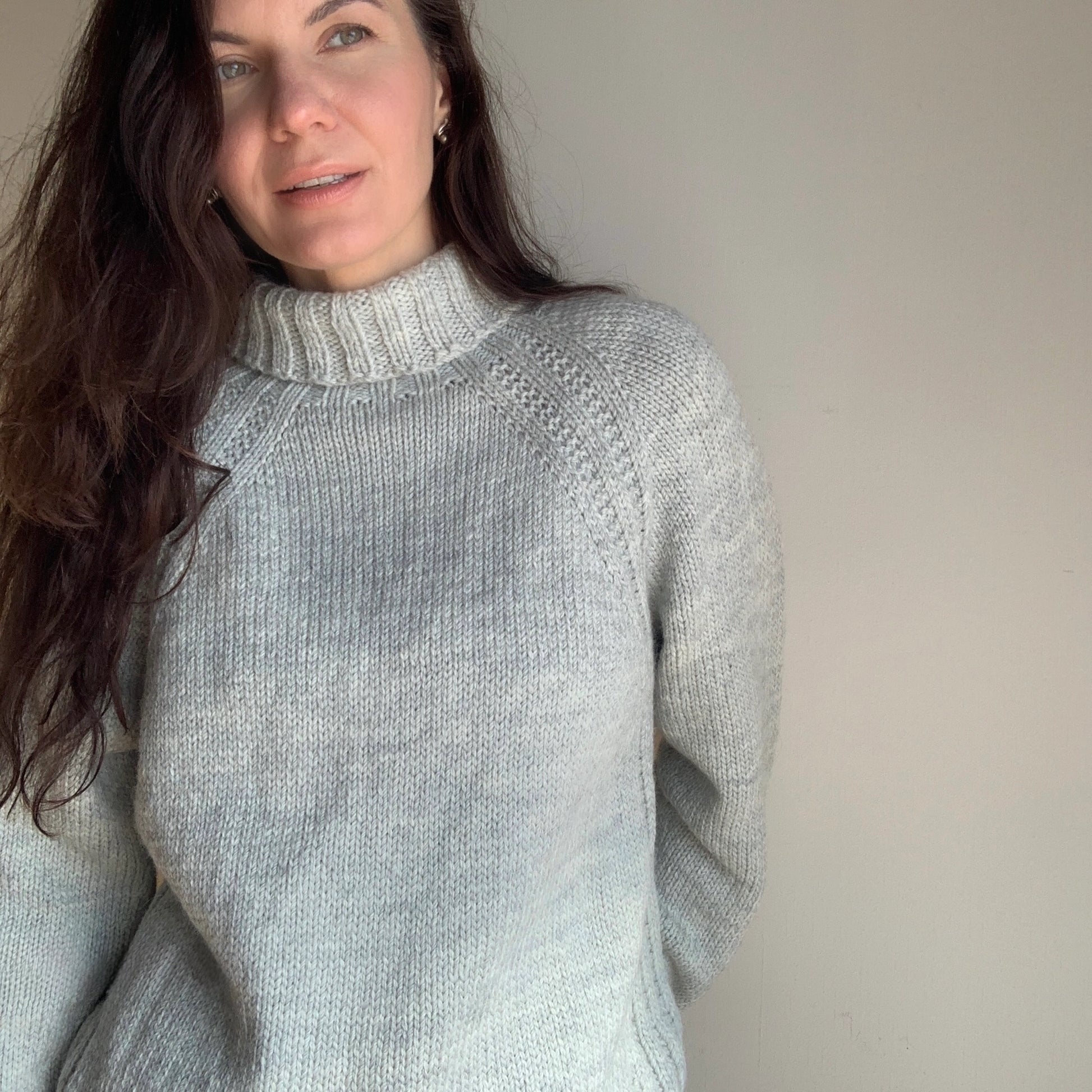 Woman wearing a light gray knit sweater against a plain background