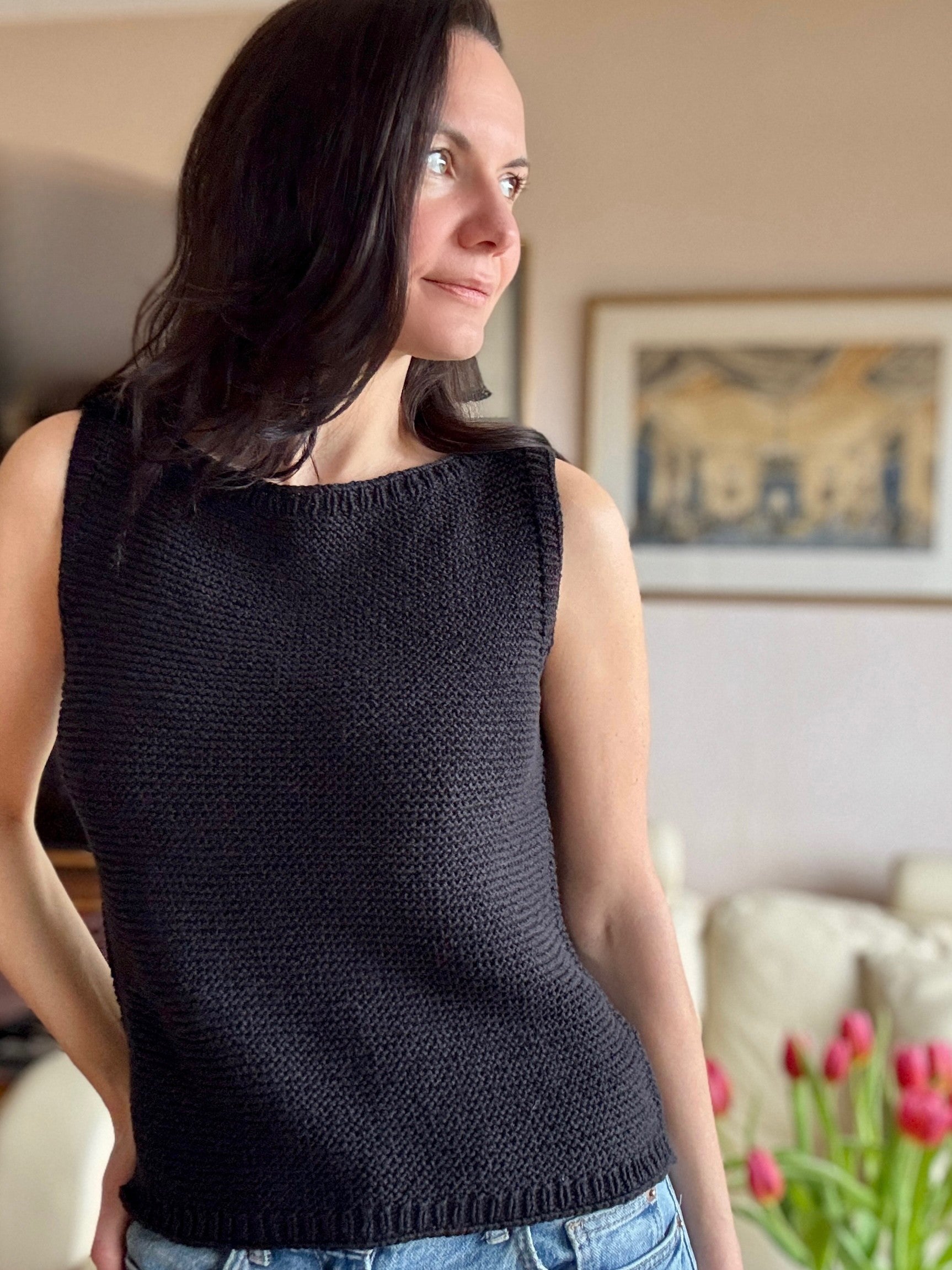 Woman wearing the Summer Soul Top in black, styled with jeans. The top features a ribbed boat neckline and hem, wide shoulder straps, and a textured garter stitch pattern. 
